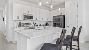 A modern kitchen with white cabinetry, stainless steel appliances, and a central island with bar stools. - 3 BR, 2.5 BA Villa | Sleeps 8! (Davenport)