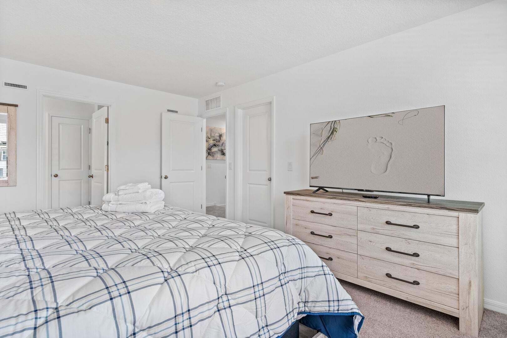 Un dormitorio con cama, cómoda, televisor y puerta que da a otra habitación.