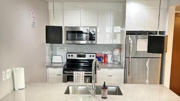 Une cuisine moderne avec des meubles blancs, des appareils en acier inoxydable et un îlot central doté de deux tabourets de bar.