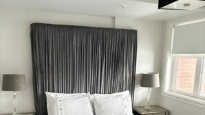 Un lit bien fait, avec du linge de lit blanc et une tête de lit grise, dans une chambre d’hôtel.