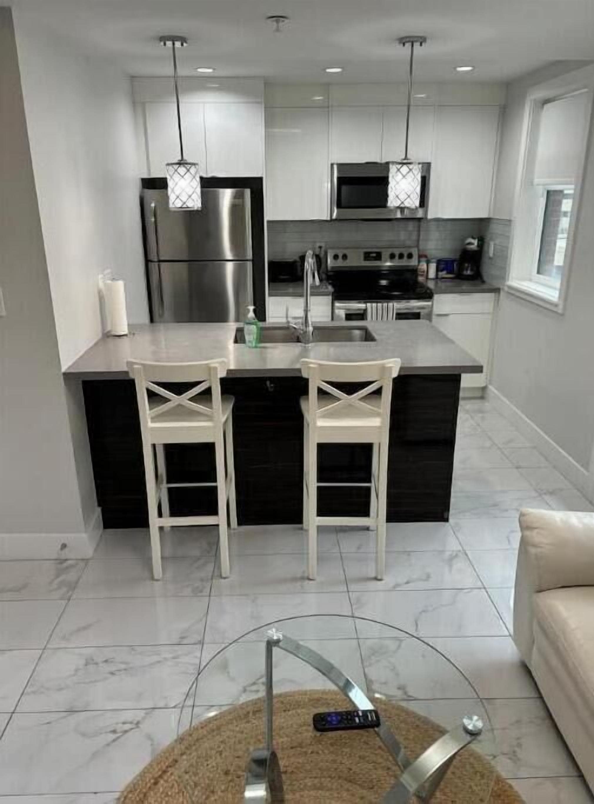 Una cocina moderna con electrodomésticos de acero inoxidable, una isla central con taburetes altos e iluminación colgante.