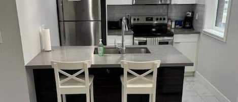 Una cocina moderna con electrodomésticos de acero inoxidable, una isla central con taburetes altos e iluminación colgante.