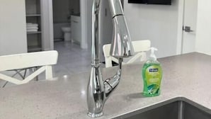 A modern kitchen with a stainless steel sink, a white countertop, and a green bottle of dish soap.