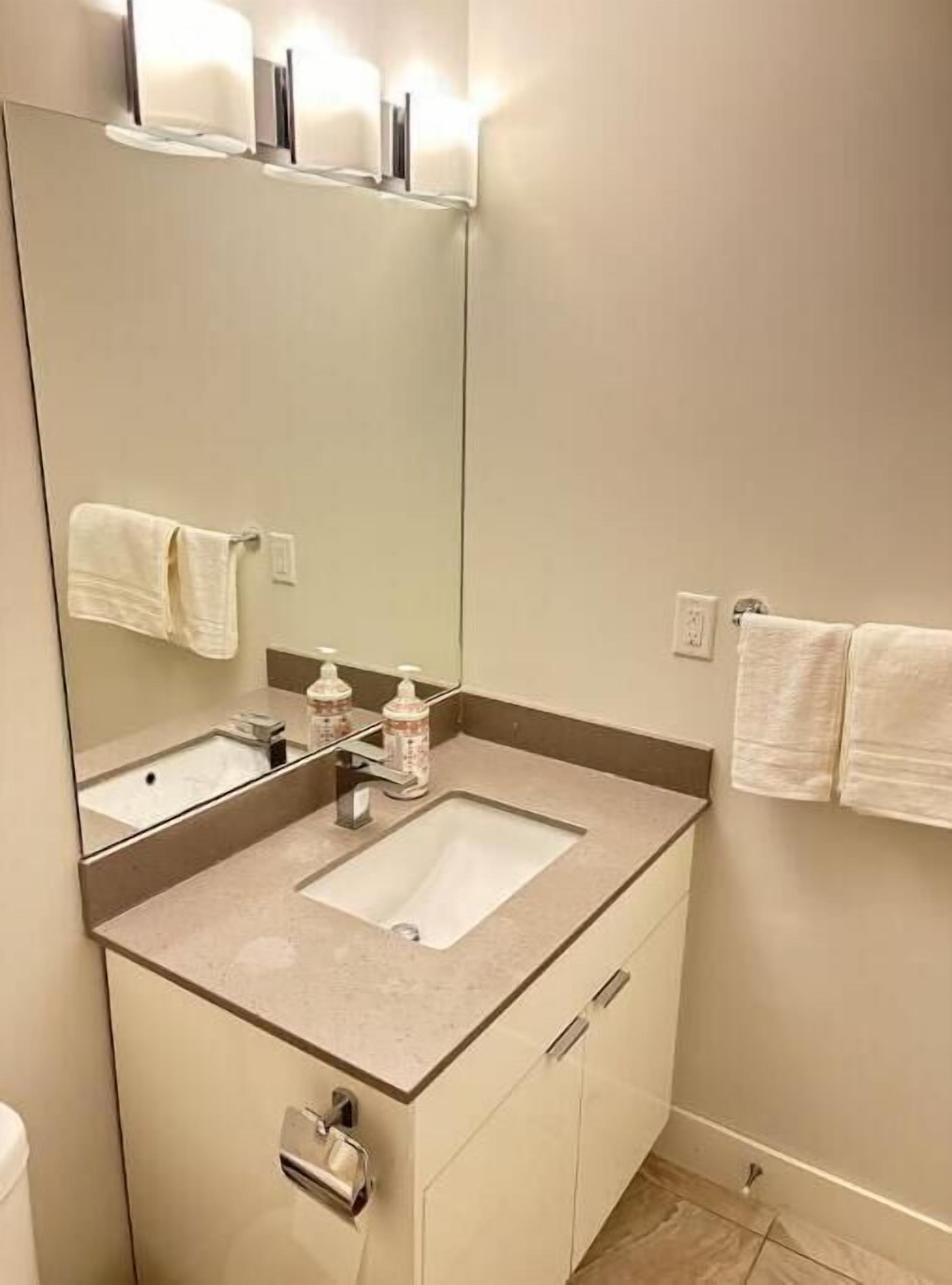 A bathroom with a large mirror, a sink, and a towel rack.
