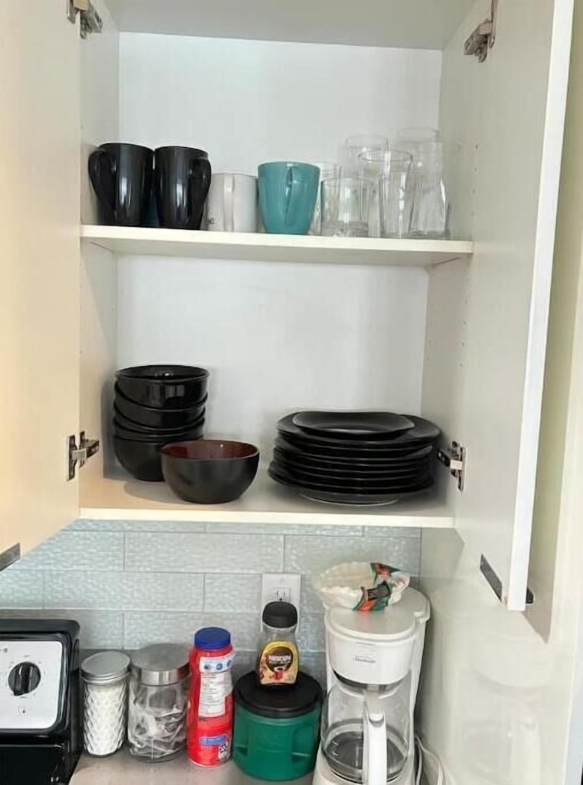 Een keuken met witte kasten, zwart en teal servies en diverse keukenapparaten.