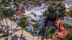 A multi-story hotel with balconies, a beach area with sun loungers, and palm trees. - Comfortable & Safe Bavaro Beach Studios (Punta Cana)