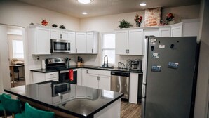 A modern kitchen with white cabinets, stainless steel appliances, and a central island with bar stools. - Amazing 6 bdrm Downtown KC/Near Plaza/UMKC (Kansas City)