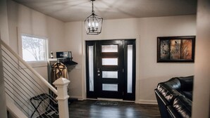 A hallway with a staircase, a black door with frosted glass panels, a black leather couch, and a ceiling light fixture. - Amazing 6 bdrm Downtown KC/Near Plaza/UMKC (Kansas City)