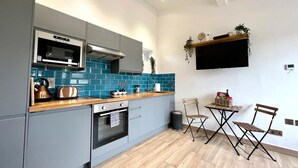 Une cuisine moderne avec des meubles gris, un pare-feu en carreaux bleus, un plan de travail en bois, un four encastré, un four à micro-ondes et un petit coin repas avec une table et deux chaises.