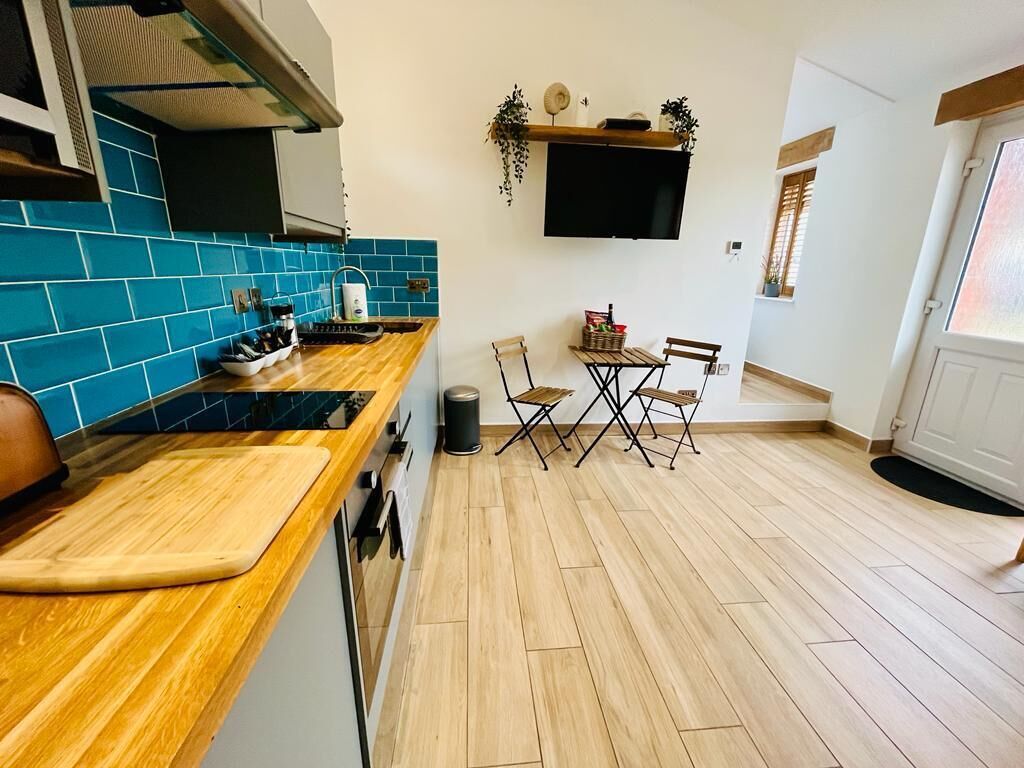 Une cuisine compacte avec des carreaux bleus, un plan de travail en bois et un coin repas comprenant deux chaises et une table.