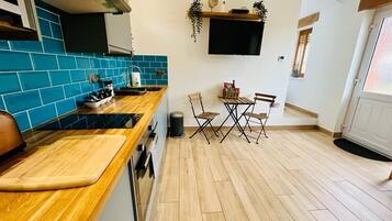 Une cuisine compacte avec des carreaux bleus, un plan de travail en bois et un coin repas comprenant deux chaises et une table.