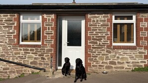 Un bâtiment en pierre avec une porte blanche et deux fenêtres dotées de volets.