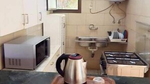A compact kitchen with a microwave, kettle, and gas stove. There is a window with a view of greenery, a sink, and a water heater.