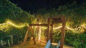 A wooden swing set with a slide in a garden at night.