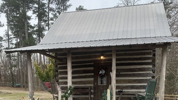 A rustic log cabin with a porch, a stone pathway leading to the entrance, and a small garden area with a bird feeder. - Got Cabin Fever? - Grumpy Ol' Goat (Pleasant Garden)