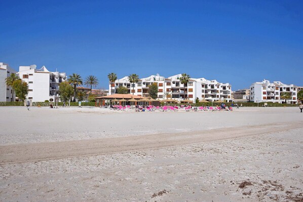 A beachfront hotel with multiple balconies, palm trees, and beach chairs.
