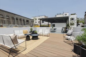 Une terrasse sur le toit, dotée d’un espace extérieur avec des chaises et des tables, entourée de plantes en pot et agrémentée d’une pergola.