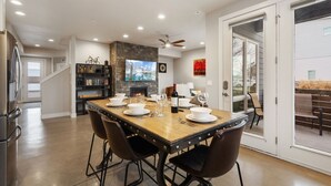 A dining area with a wooden table set for four, a fireplace, and a bookshelf. - Elegant Oasis - Fireplaces, King Beds, Mtn Views! (Fort Collins)