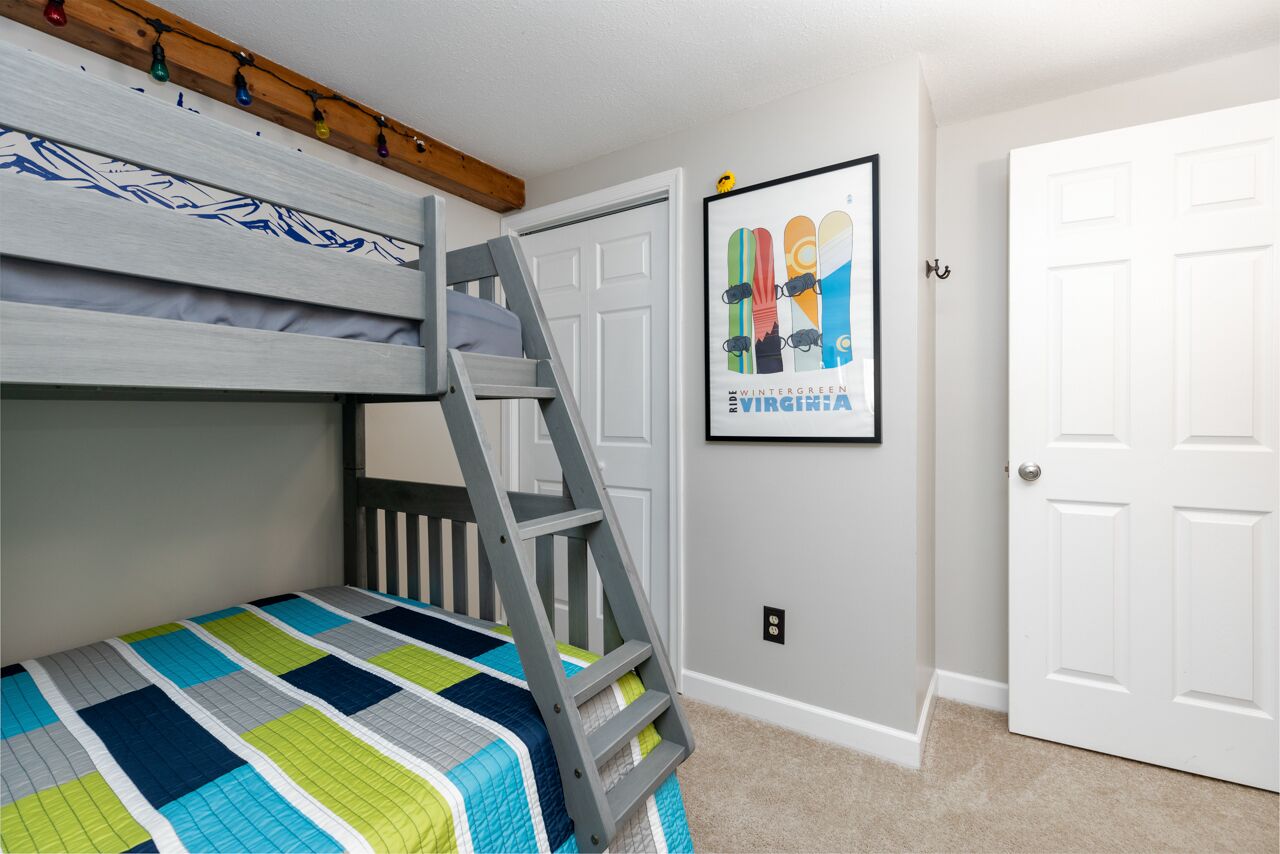 Habitación infantil con literas, una escalera, colcha colorida y un póster enmarcado en la pared.