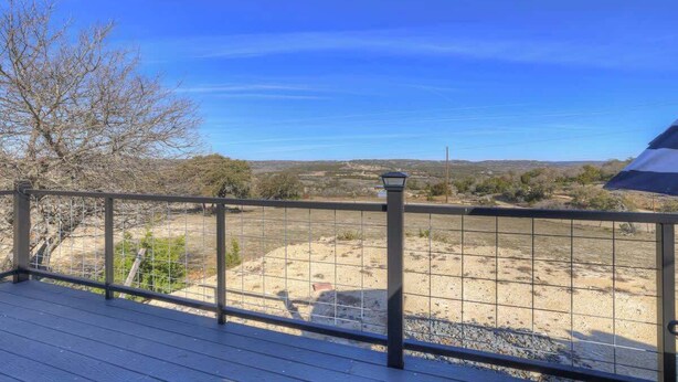 Una terraza de madera con barandilla metálica, con vistas a un paisaje seco y vegetación escasa bajo un cielo azul despejado.