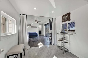 A modern hotel room with a large mirror, a bed, a small seating area, a ceiling fan, and a view of the outdoors.