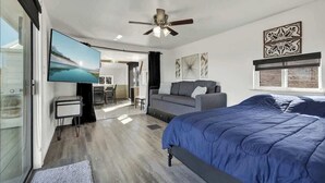 Un dormitorio moderno con una cama grande, un televisor de pantalla plana, un ventilador de techo y vista a un lago por la ventana.