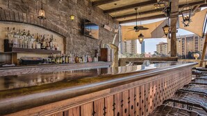 Un bar avec un mur en pierre, un comptoir en bois et des tabourets de bar en osier.
