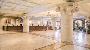 Un hall d’entrée spacieux avec un comptoir d’accueil, de grandes colonnes et un lustre.