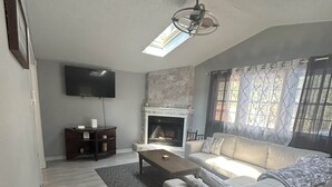 Ett vardagsrum med en soffa, ett soffbord, en öppen spis, en tv och en takfläkt.