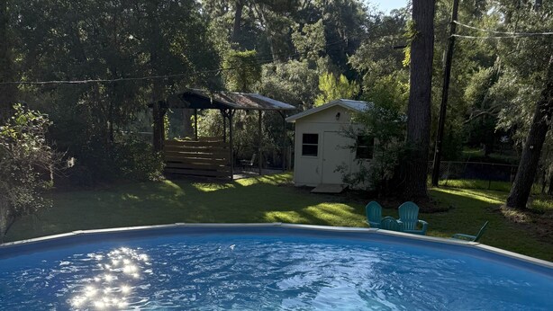 En klar och ren pool omgiven av träd och en liten byggnad.