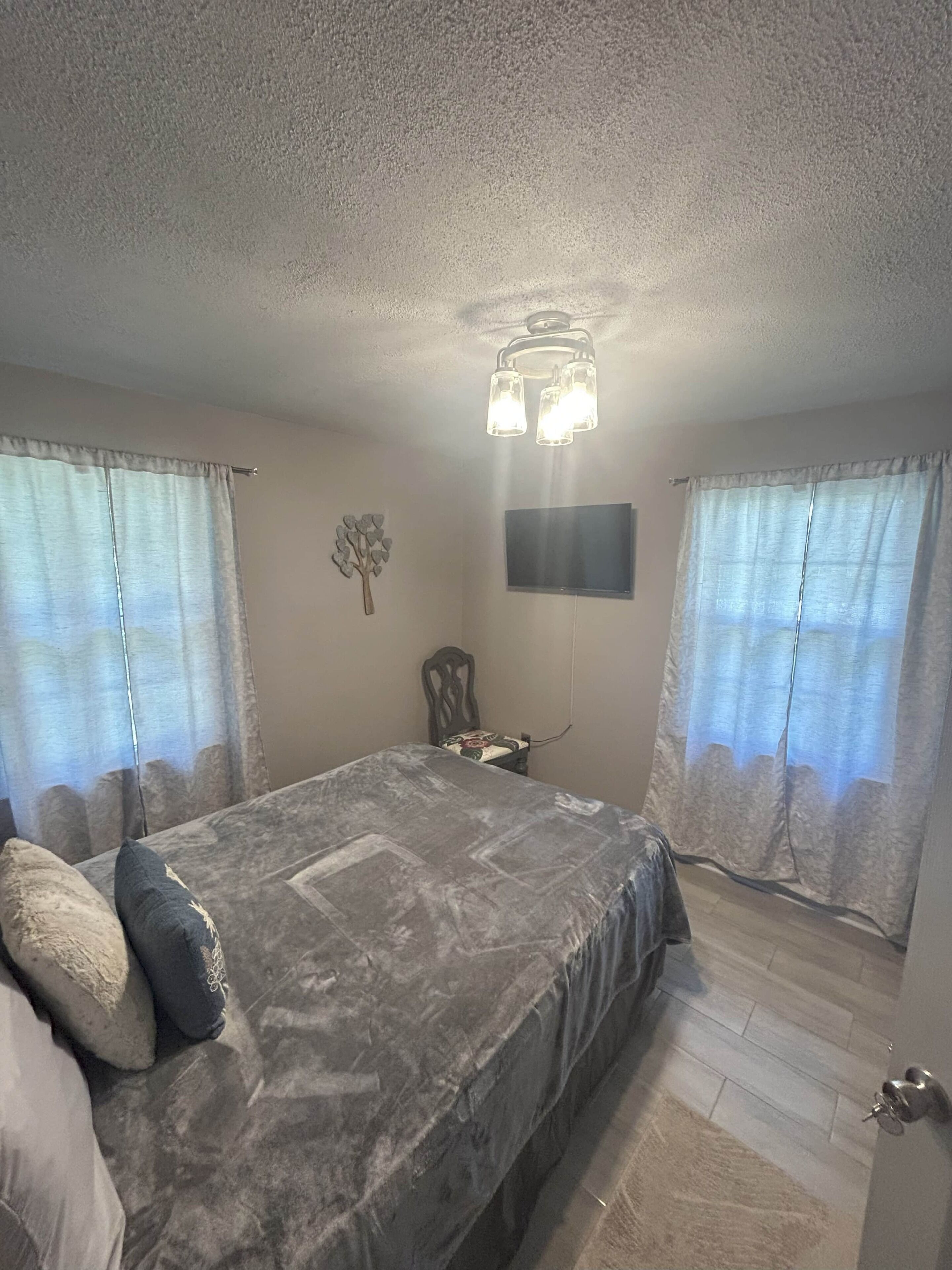 Une chambre à coucher avec un lit, des rideaux, une chaise, un téléviseur à écran plat et un luminaire au plafond.