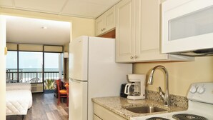 Una cocina compacta con refrigerador, estufa y microondas. Se observa un comedor con mesa y sillas al fondo.