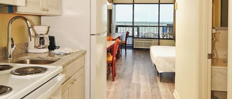 Une cuisine compacte équipée d’une cuisinière, d’un évier et d’un réfrigérateur, donnant sur un balcon avec un coin repas et un lit.