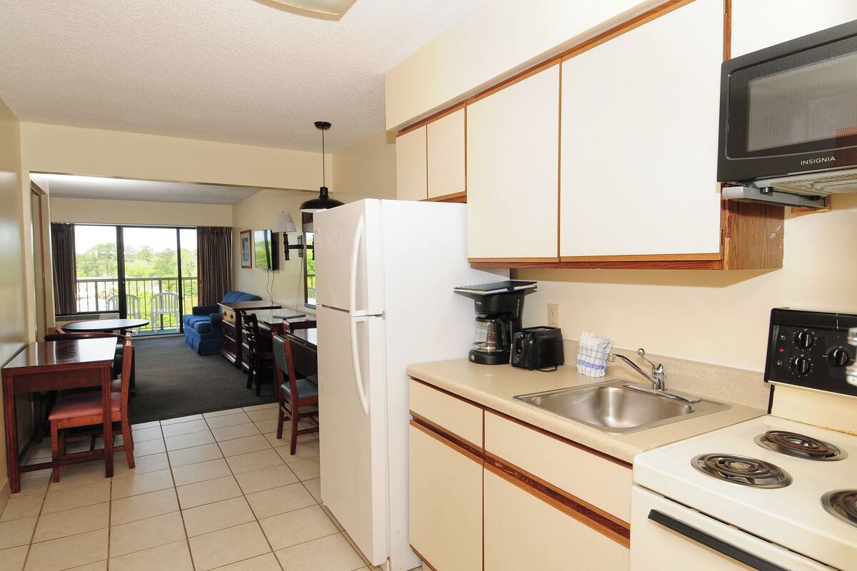 A kitchen with a refrigerator, stove, sink, and a microwave. There is a dining table and chairs in the adjacent dining area.