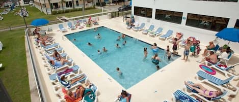 Un espace piscine doté de chaises longues et de parasols, entouré d’un bâtiment avec des balcons.