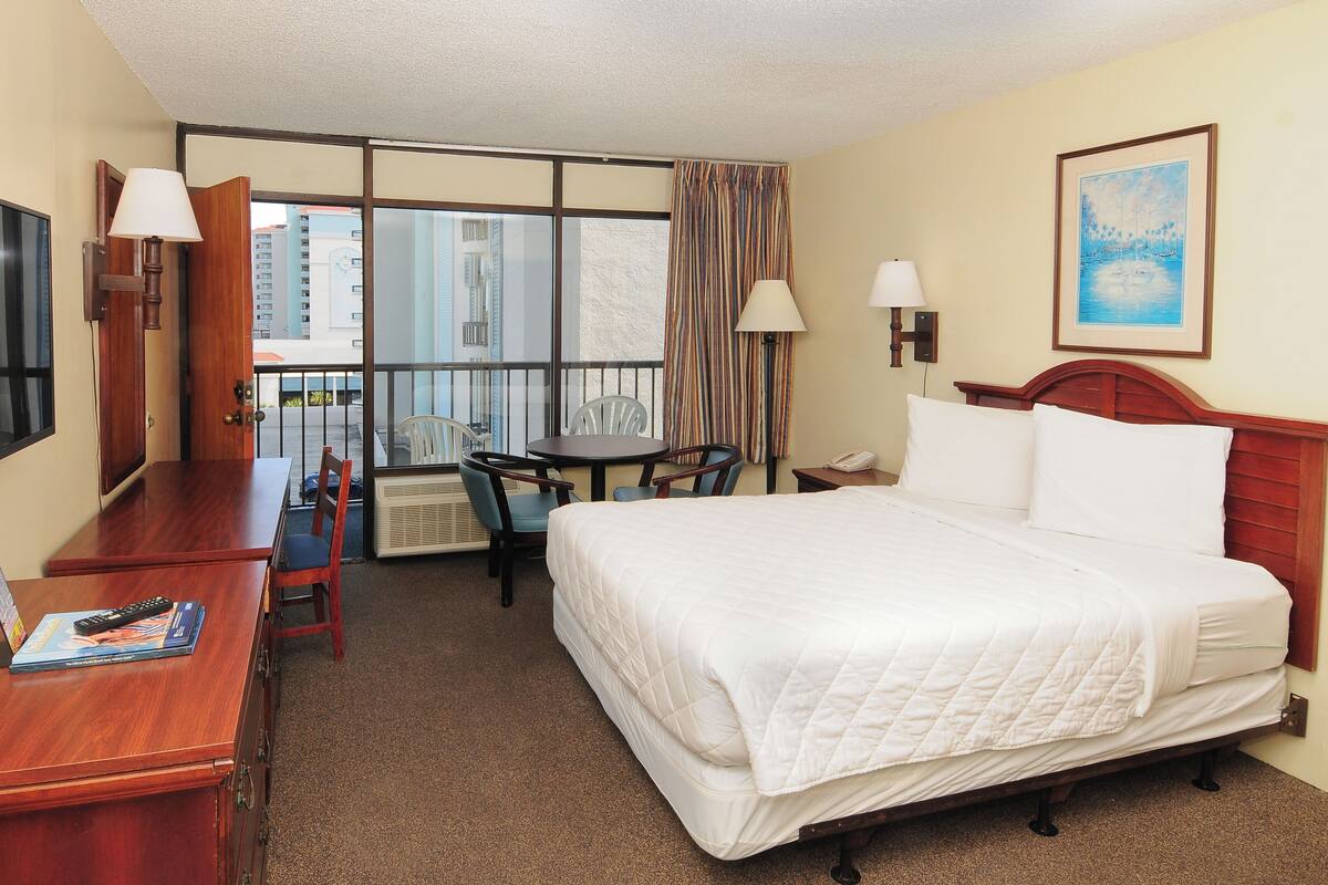 A hotel room with a bed, a desk, a chair, a TV, and a window with curtains.