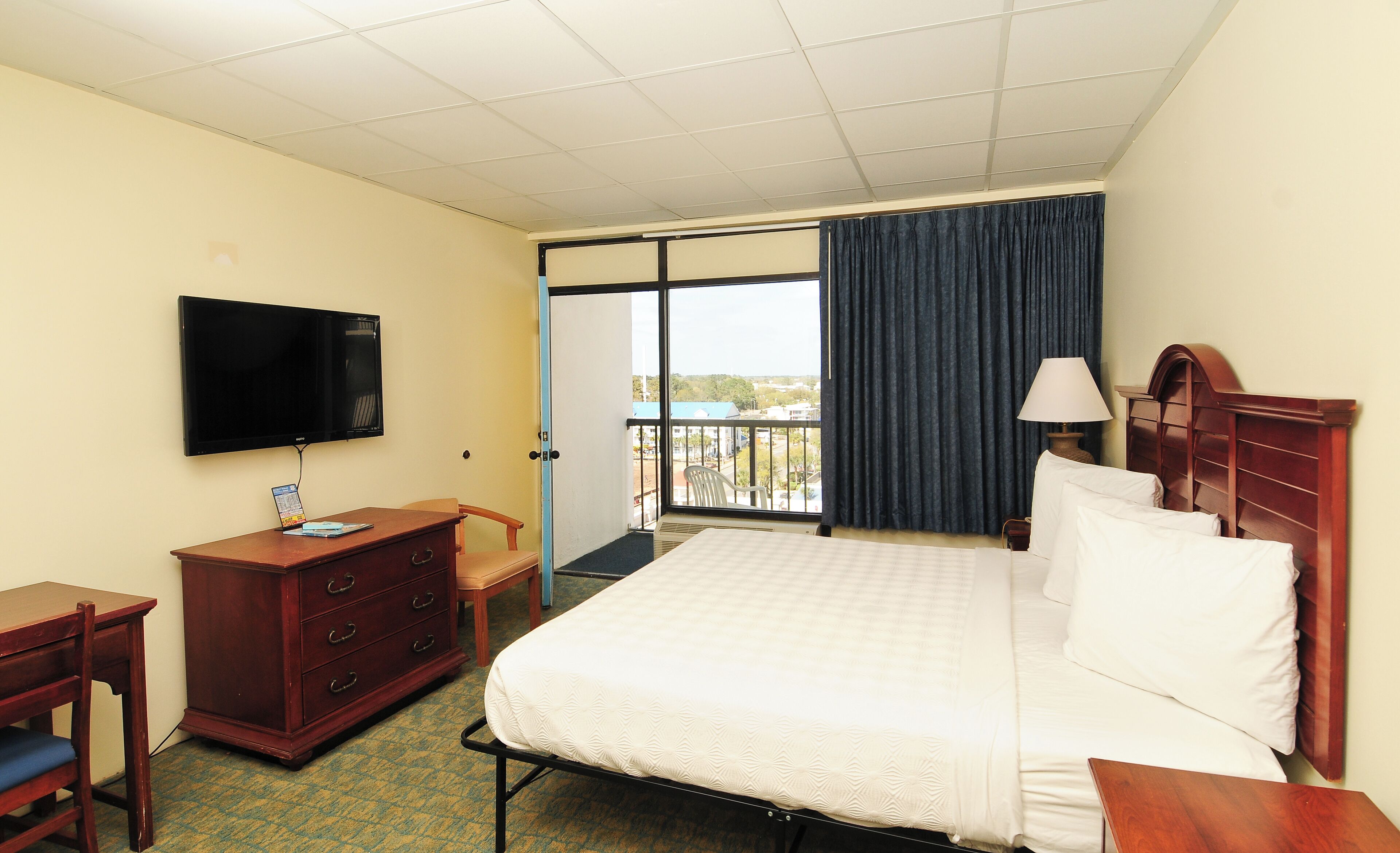 A hotel room with a bed, a desk, a chair, a television, and a balcony with a view.