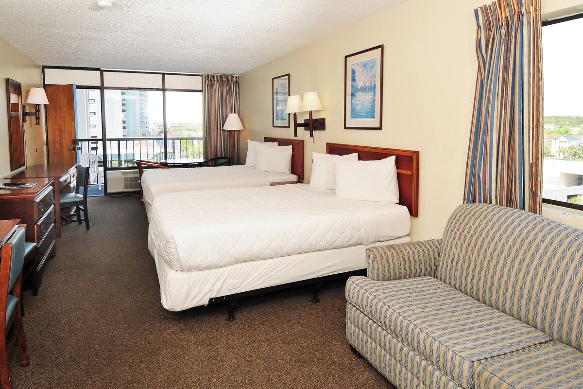 A hotel room with two beds, a sofa, a desk, and a chair.