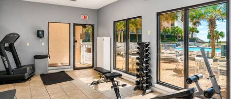 A gym with exercise equipment, a treadmill, and a view of a pool and palm trees.