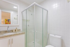 Ein modernes Badezimmer mit einer Glaskabine zur Dusche, einem weißen Waschbecken und einer Toilette.