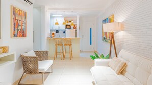 Una sala de estar moderna con un sofá blanco, sillas de mimbre y una zona de comedor con una cocina al fondo.