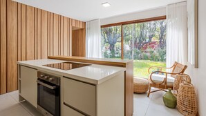 Une cuisine moderne avec un îlot central, un lambris en bois sur le mur et une grande fenêtre donnant sur un paysage verdoyant, avec une enseigne Coca-Cola visible.