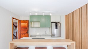 Une cuisine moderne dotée d’un îlot central, de meubles verts, d’un réfrigérateur en acier inoxydable et d’éléments décoratifs en bois.