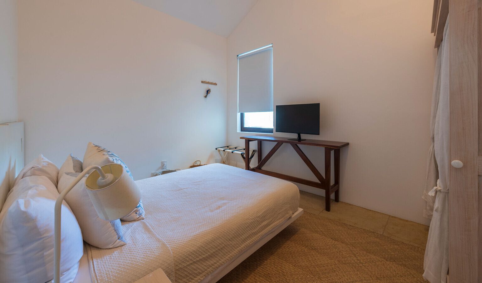 A bedroom with a bed, a bedside table, a TV, and a window.