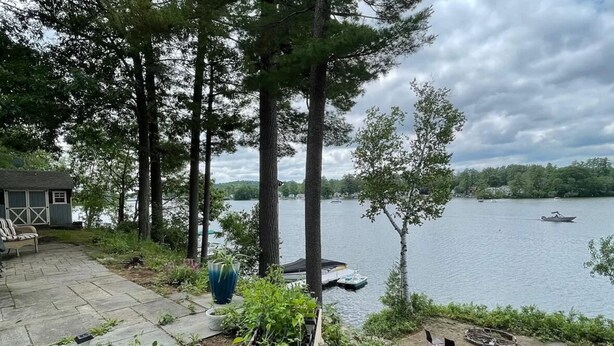 A lakeside patio with a stone deck, a wooden planter with plants, a grill, and a view of the lake with boats. - Lake Winnisquam water front home  (Belmont)