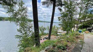 A lakeside view with a paved walkway, trees, and a distant dock. - Lake Winnisquam water front home  (Belmont)