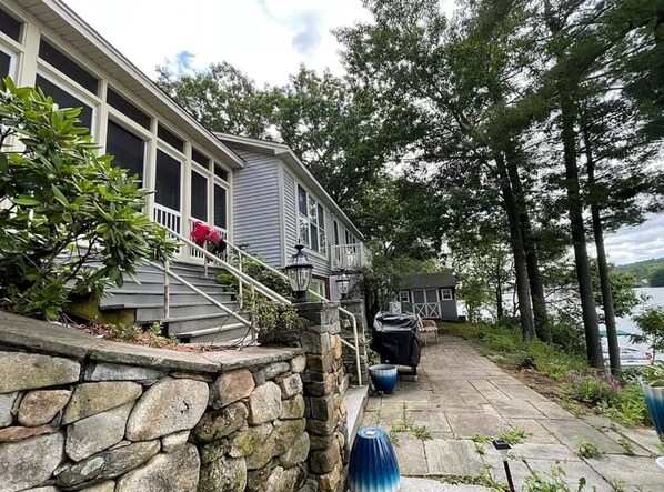 A stone wall, a porch, and a pathway leading to a house with a covered grill area.