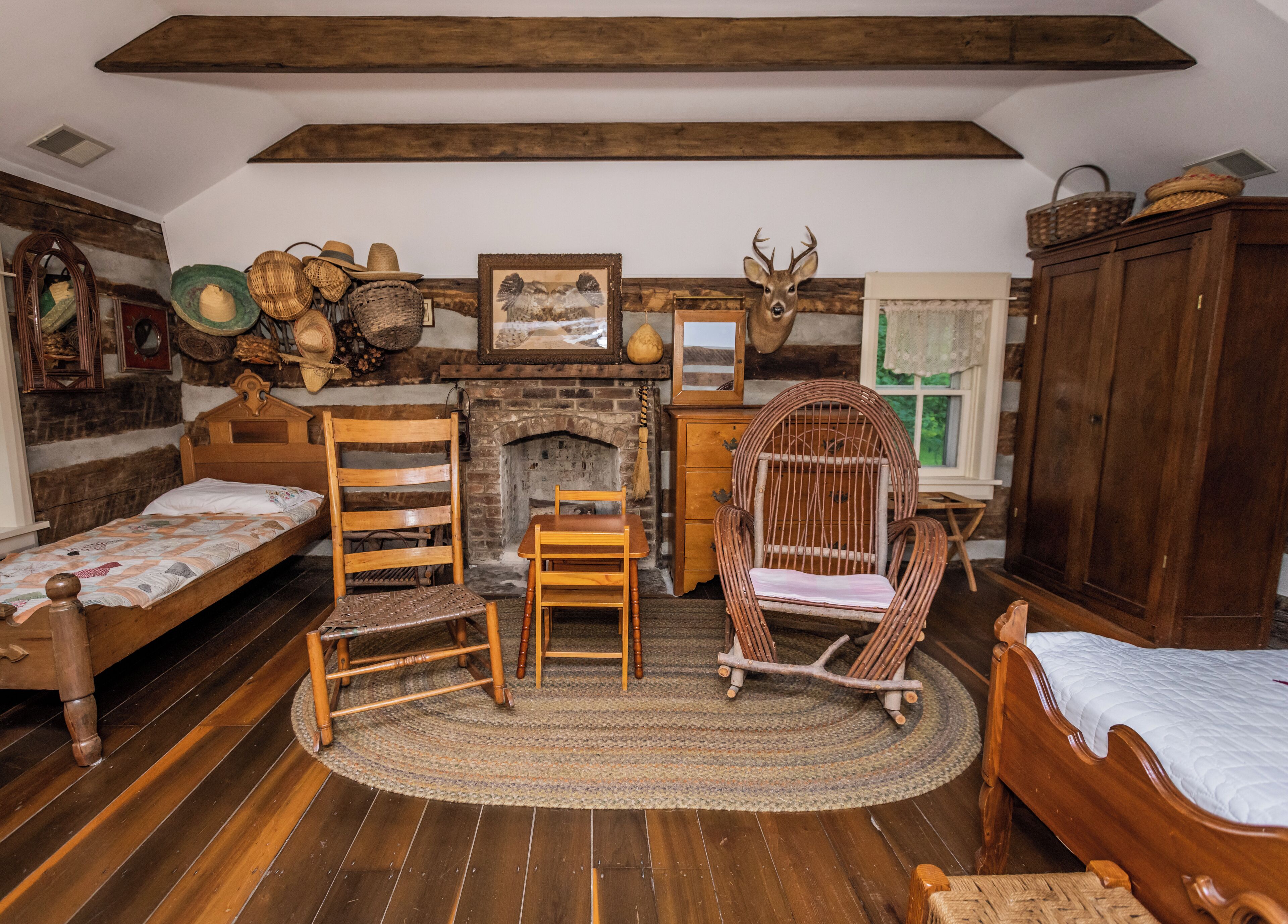 A rustic room with a wooden bed, a wooden chair, a rocking chair, a fireplace, and a deer head decoration.