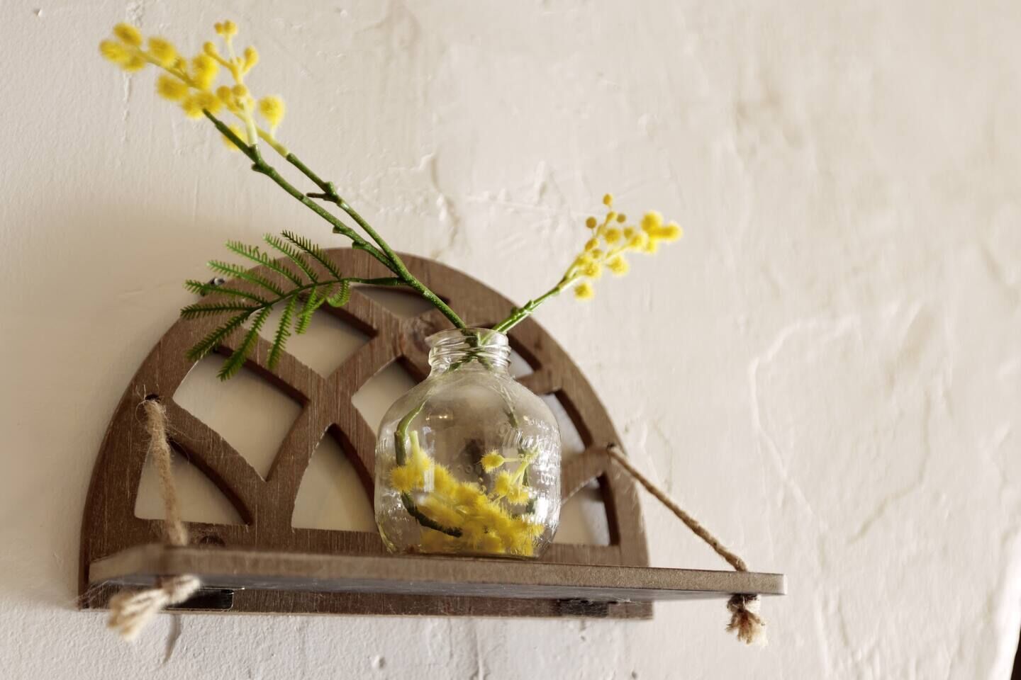 Un bocal en verre transparent contenant des fleurs jaunes, posé sur une étagère en bois fixée au mur.