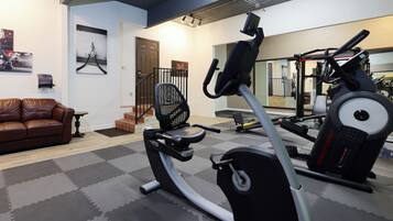 A home gym with exercise equipment, a brown leather couch, and a mirror reflecting the gym area.